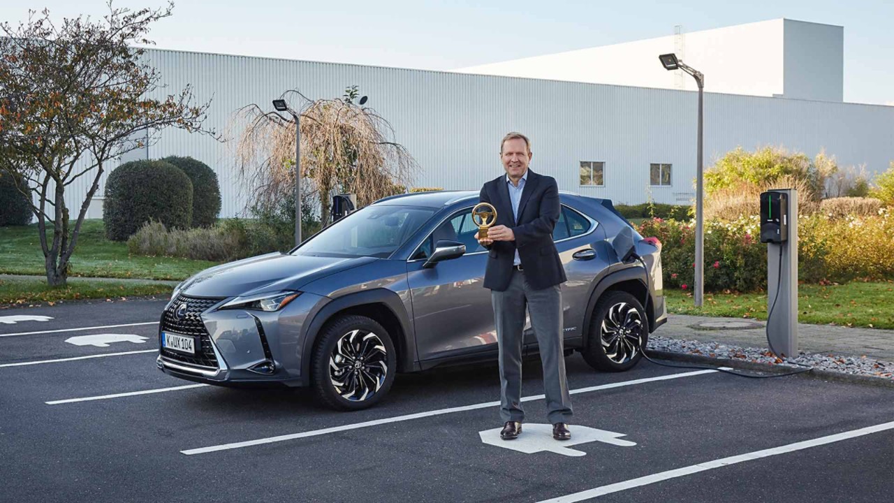 Ein Herr mit dem Preis in der Hand. vor einem Lexus UX 300e, der an einer Ladestation ist.