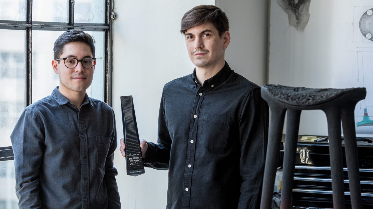Zwei Gewinner stehen nebeneinander. Der Gewinner, der auf der rechts steht hält das gewonnene Preis in der Hand.