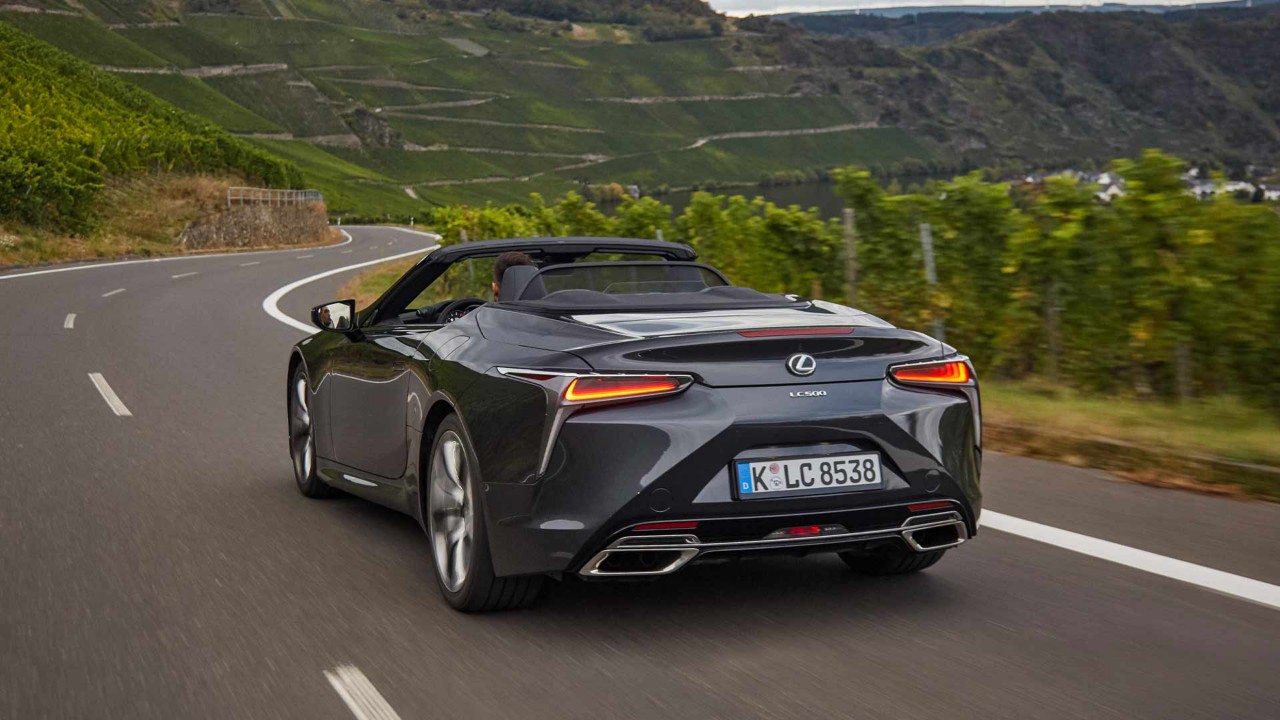 Der neue Lexus LC500 wird von hinten gezeigt und fährt auf einer schnellen Straße in grüner Umgebung.