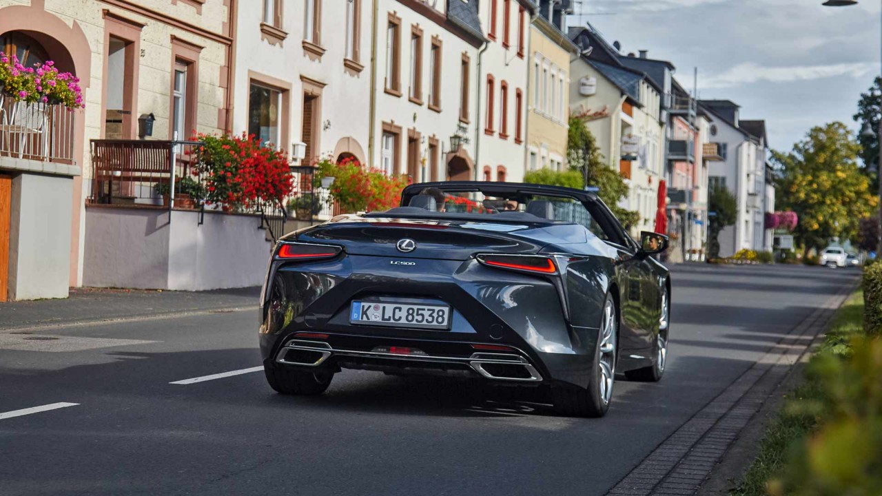 Hinteransicht des neuen  Lexus LC500 der bei Sonnenschein durch die Stadt fährt.