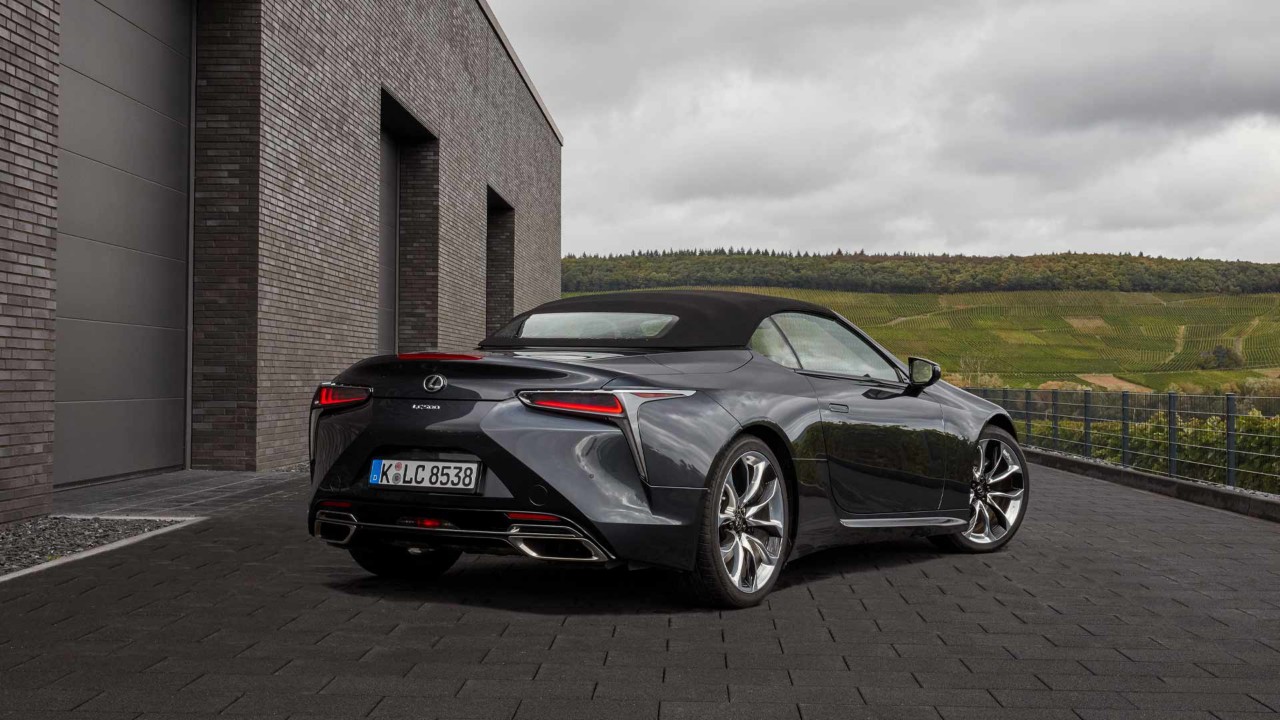 Hinteransicht des neuen Lexus LC500 der vor einem modernen Gebäude in einer grünen Umgebung steht.