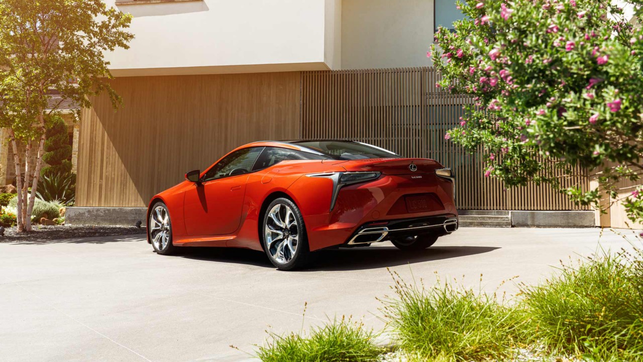 Hinteransicht eines orangenen Lexus LC Coupé vor einem modernen Wohnhaus.