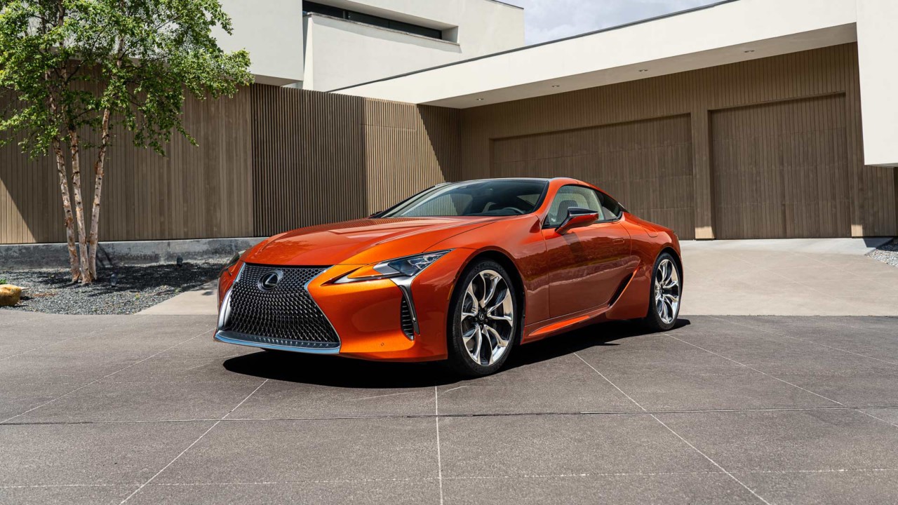 Fordere Seitenansicht eines orangenen Lexus LC Coupé vor einem modernen Wohnhaus.