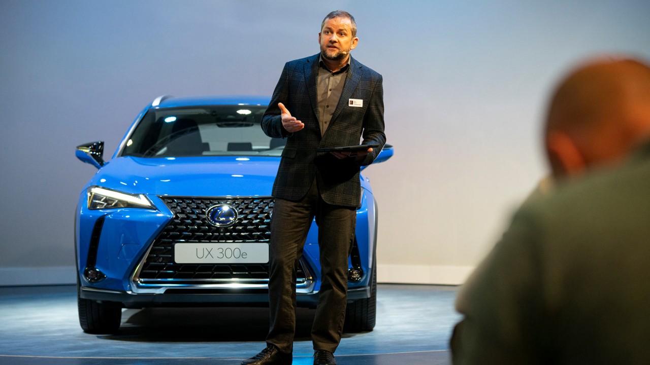 Mann steht vor Lexus ux300e und hält eine Rede